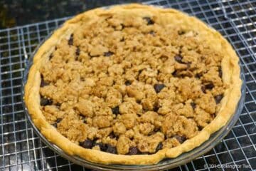 Whole blueberry crumble pie cooling on a rack.