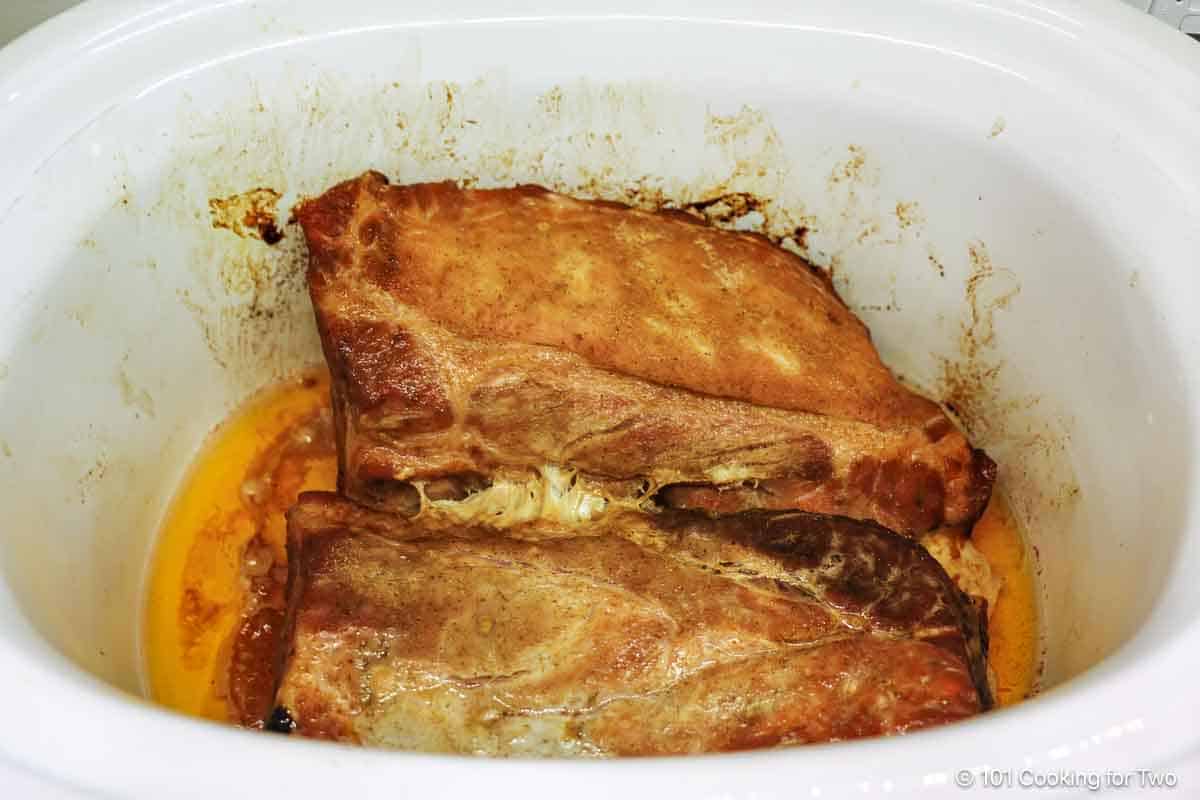 cooked ribs in crock pot with drainage.