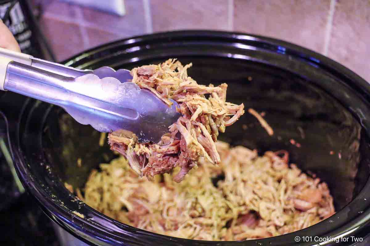 Shredded pork tenderloin in tongs.