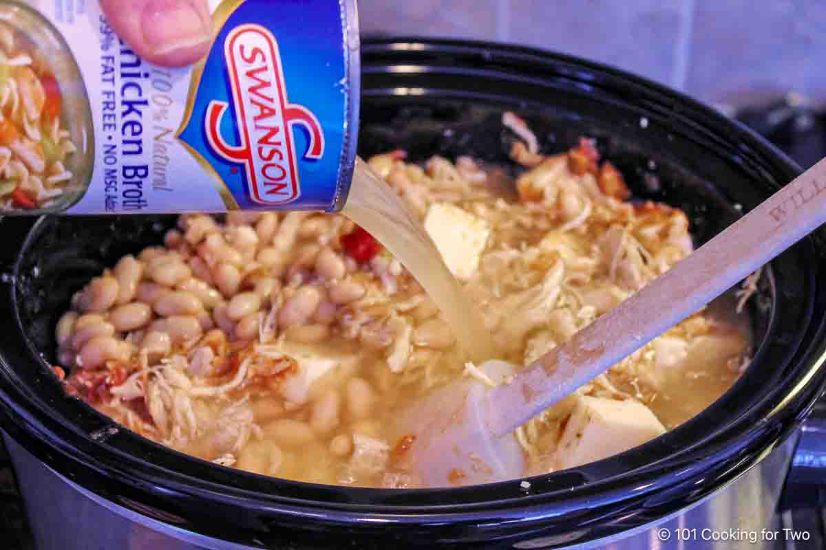 Adding broth to thin the chili.