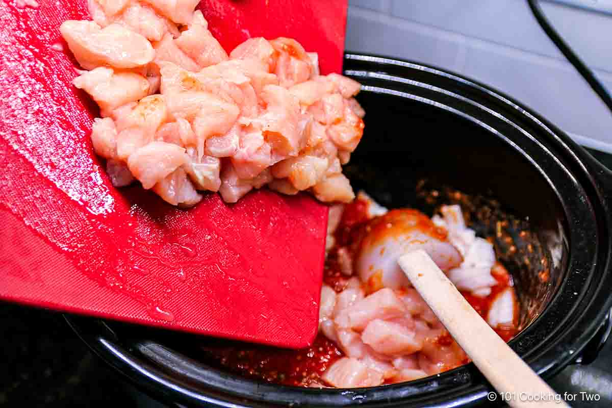 Adding chicken to sauce in the crock pot.