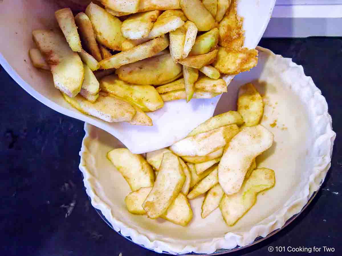 adding coated apple slices to raw pie crust.