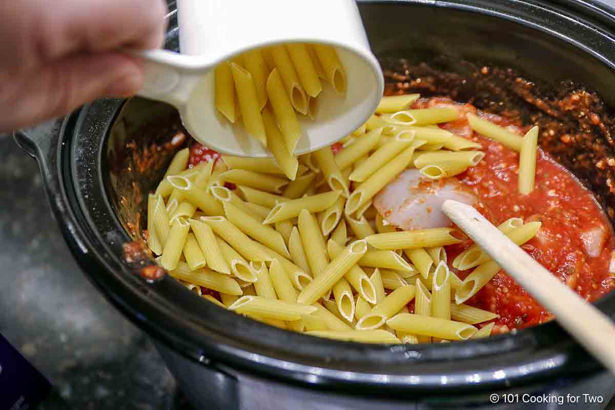 Adding dry pasta to the crock pot.