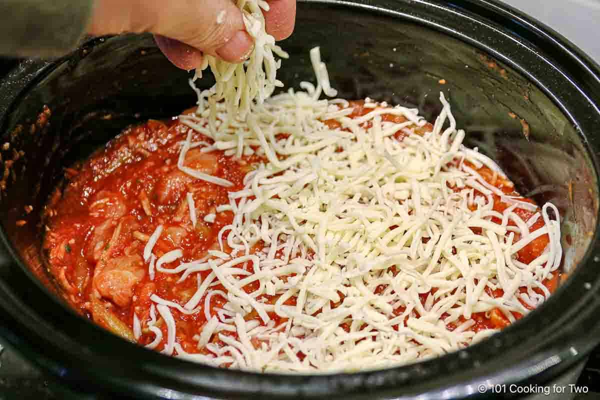 Topping the chicken pasta with shredded mozzarella cheese.