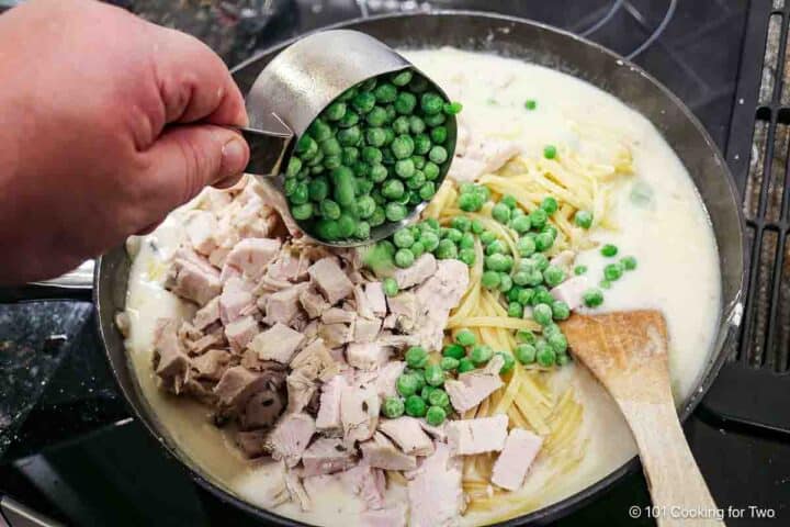 Adding frozen peas and turkey to the sauce.