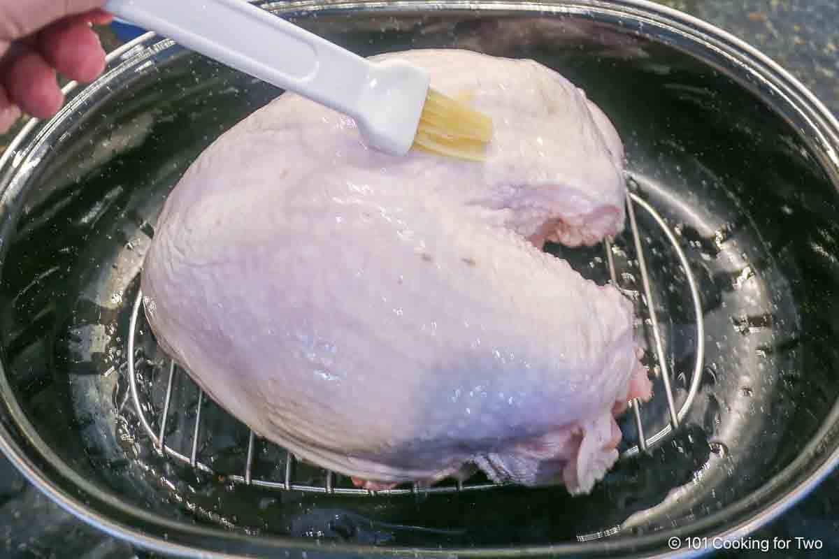 Brushing a turkey breast on a rack with oil.