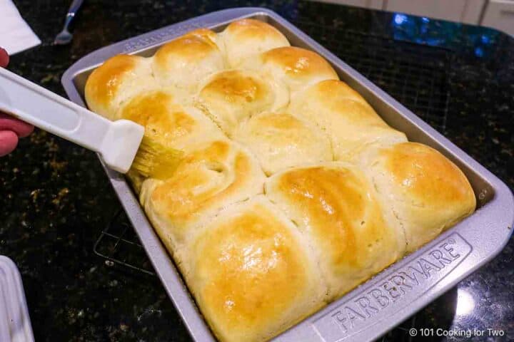 Brushing baked rolls with butter.