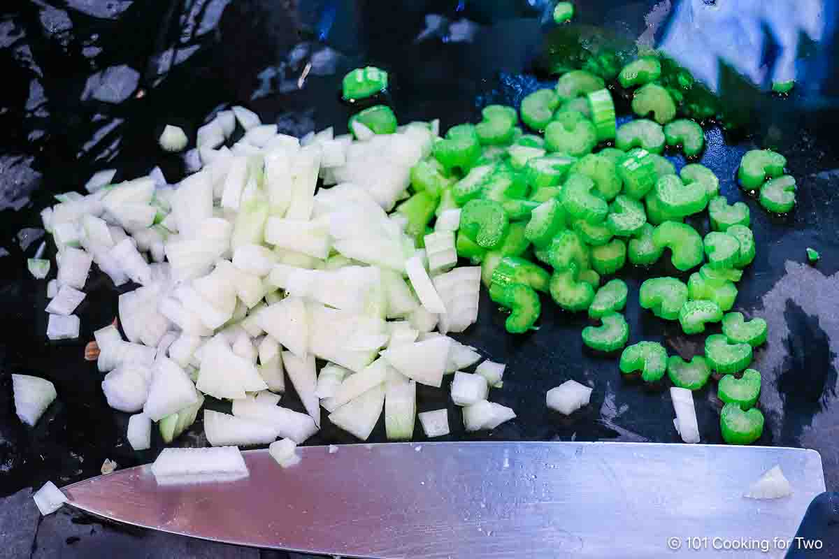 Chopped onion and celery on black board with a knife.