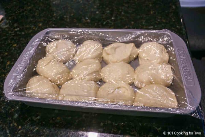 Dough balls in the baking pan with plastic wrap.