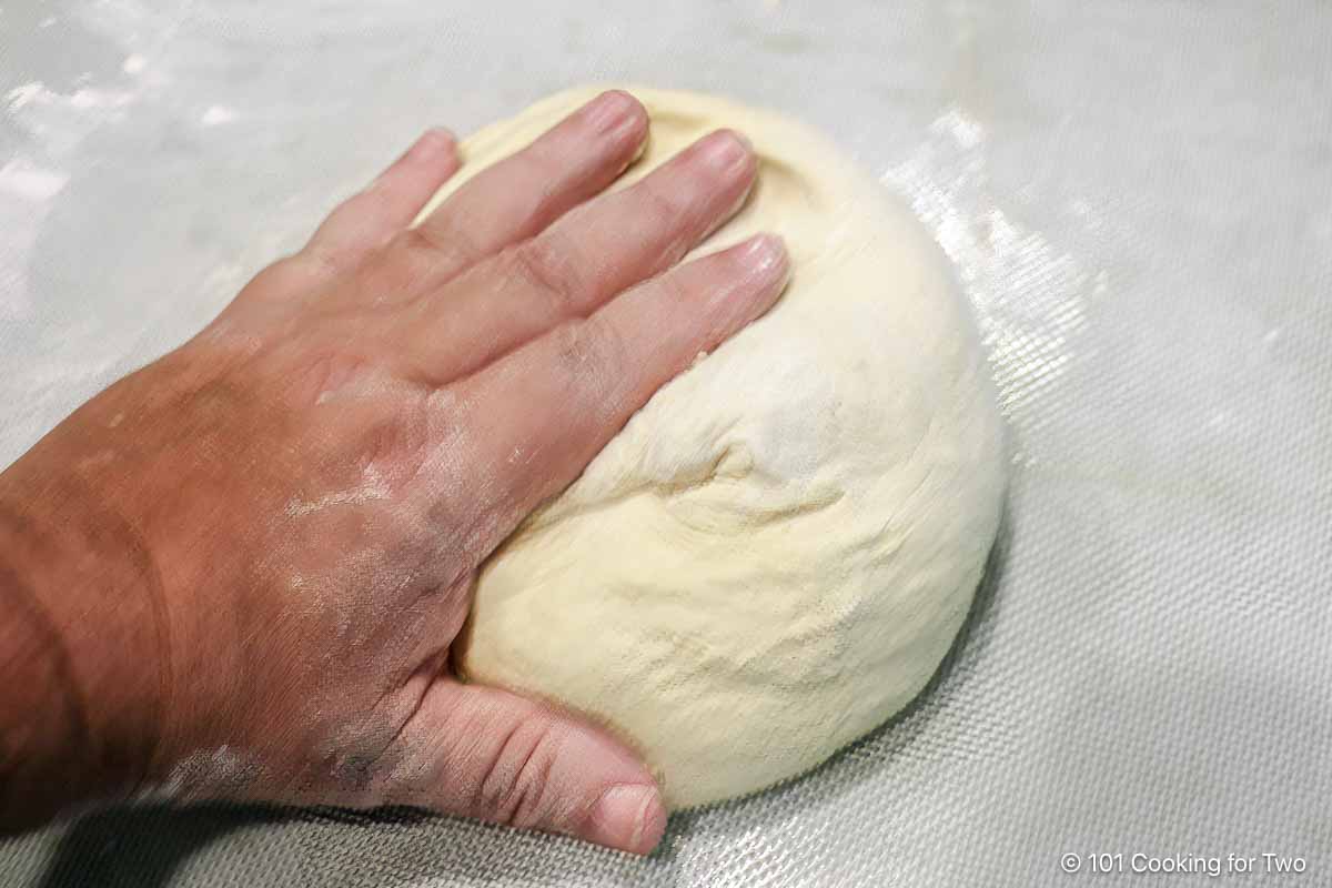 hand-kneading dough ball on a floured surface.