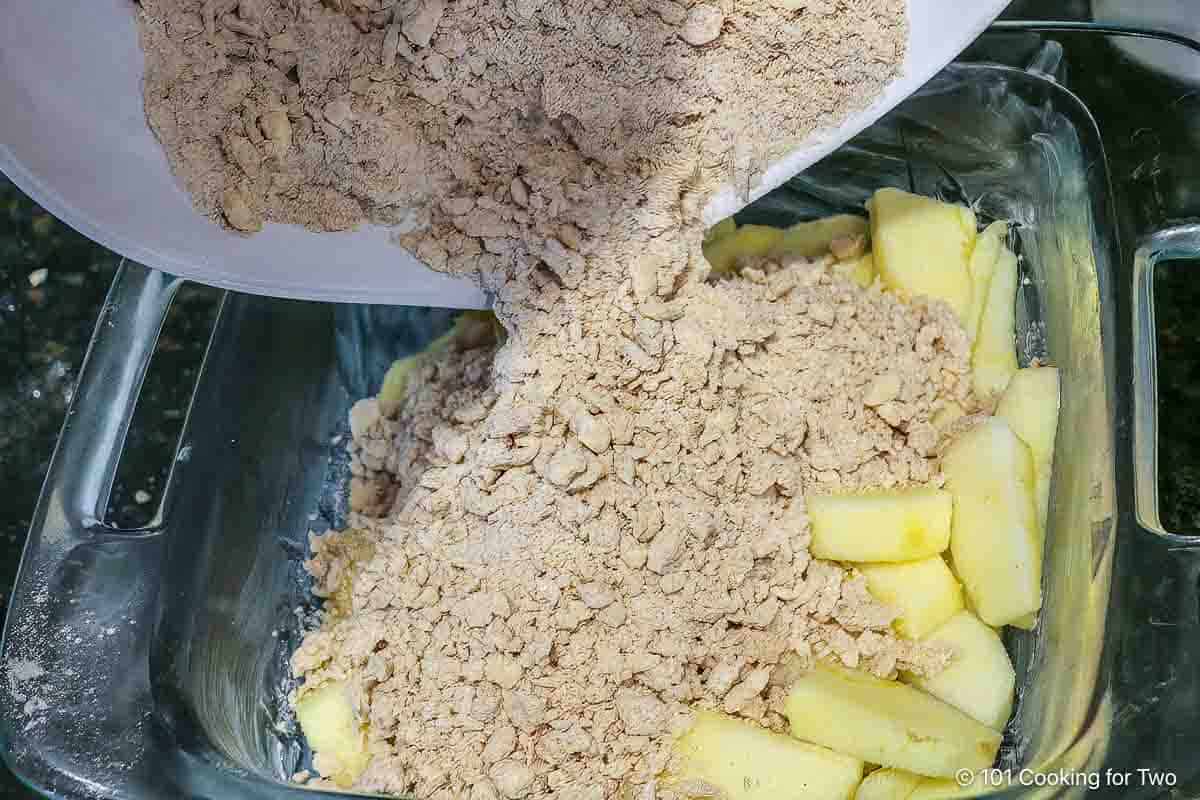 Pouring topping over sliced apples in baking dish.