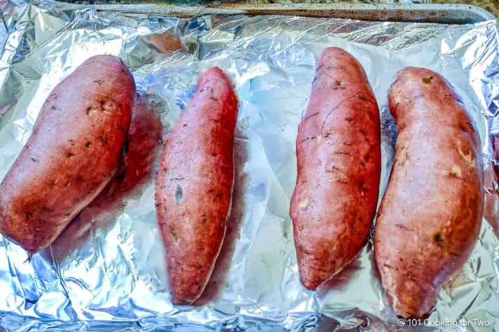 Raw sweet potatoes on a foil tray.