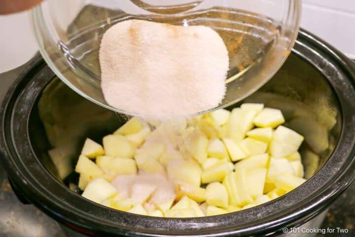 Sprinkling cinnamon sugar over apples in the crock pot.