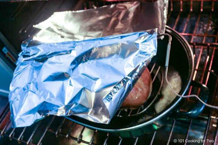 Tenting a cooking turkey breast with foil.