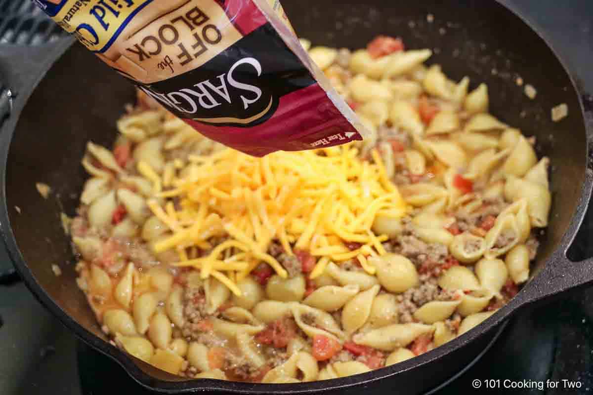 Adding cheese to the cooked chili mac.