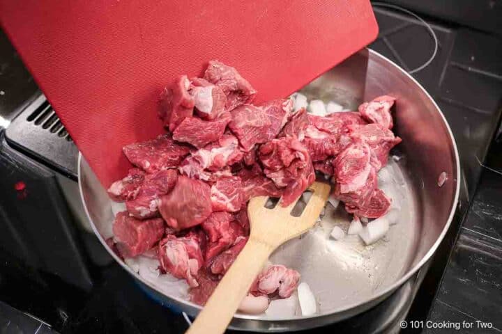 Adding meat and onion to a pan to brown