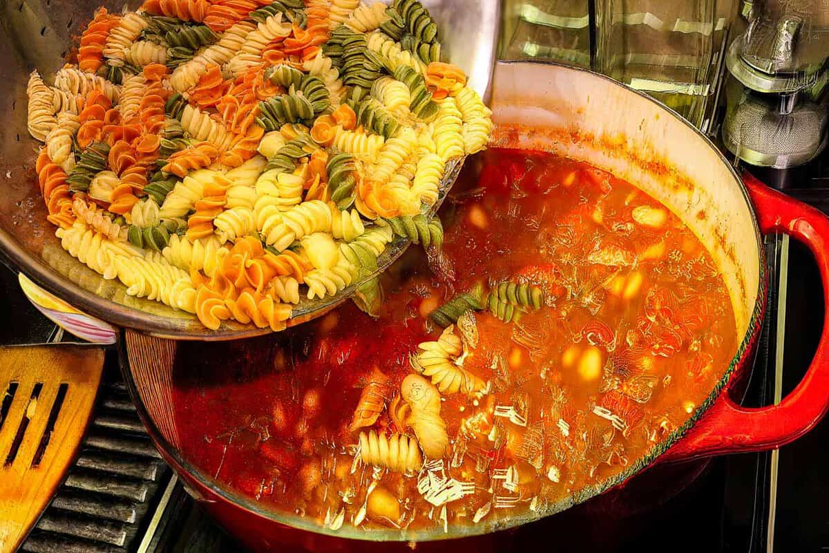 Pouring pasta into soup.