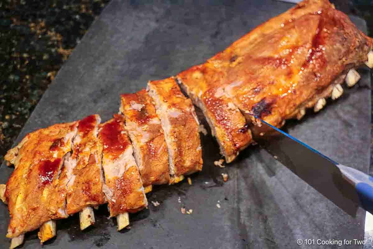 Cutting cooked baby back ribs into individual ribs.