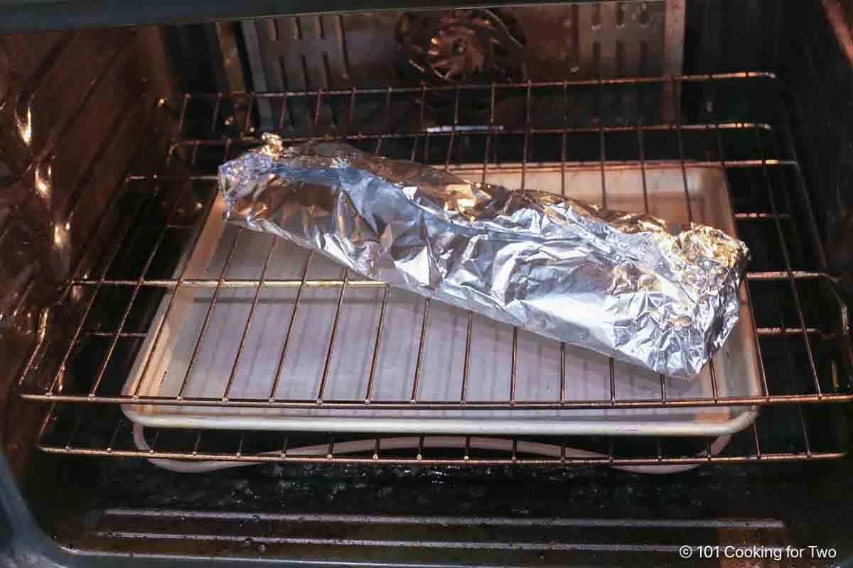 Foil wrapped ribs on a oven rack with a tray on the lower rack.