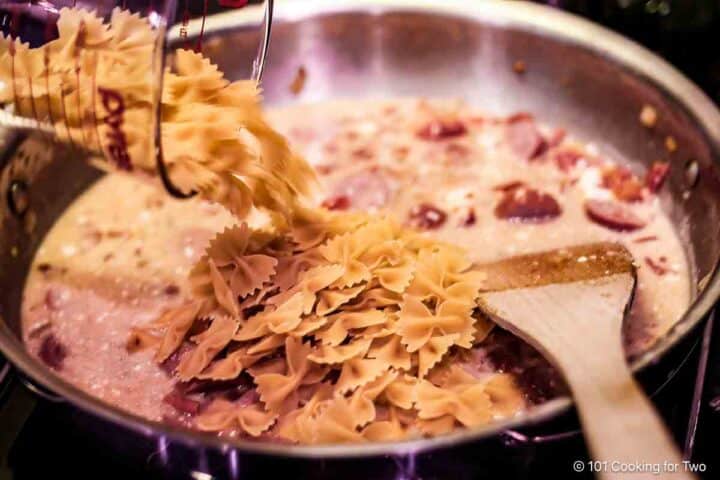 Adding bowtie pasta to the pan.