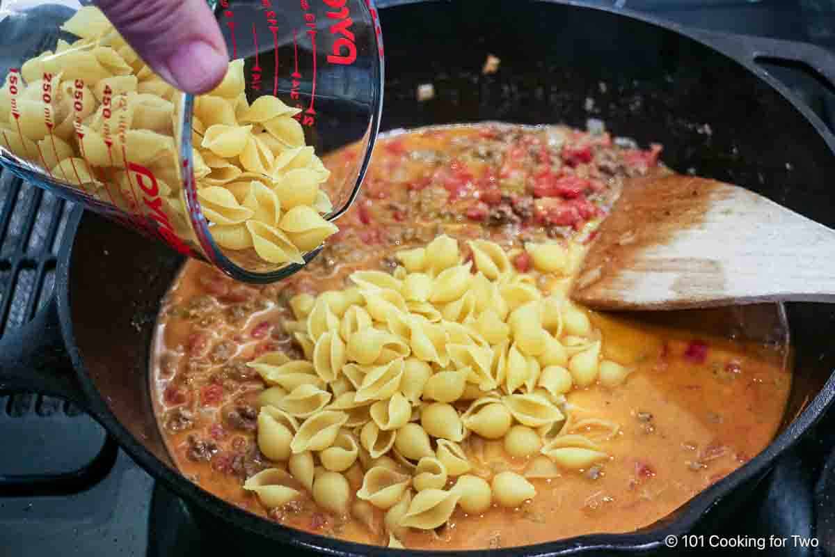 Adding dry pasta to the sauce.