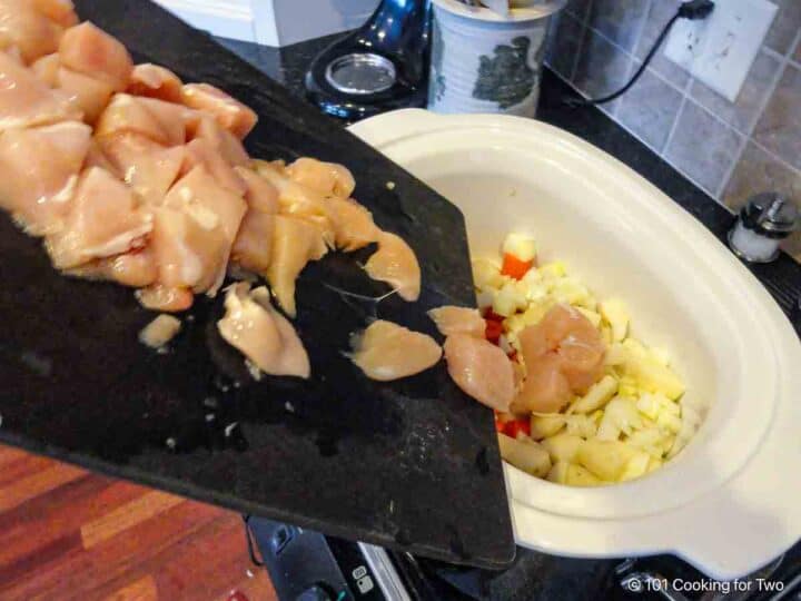 adding trimmed chicken to the crock pot.