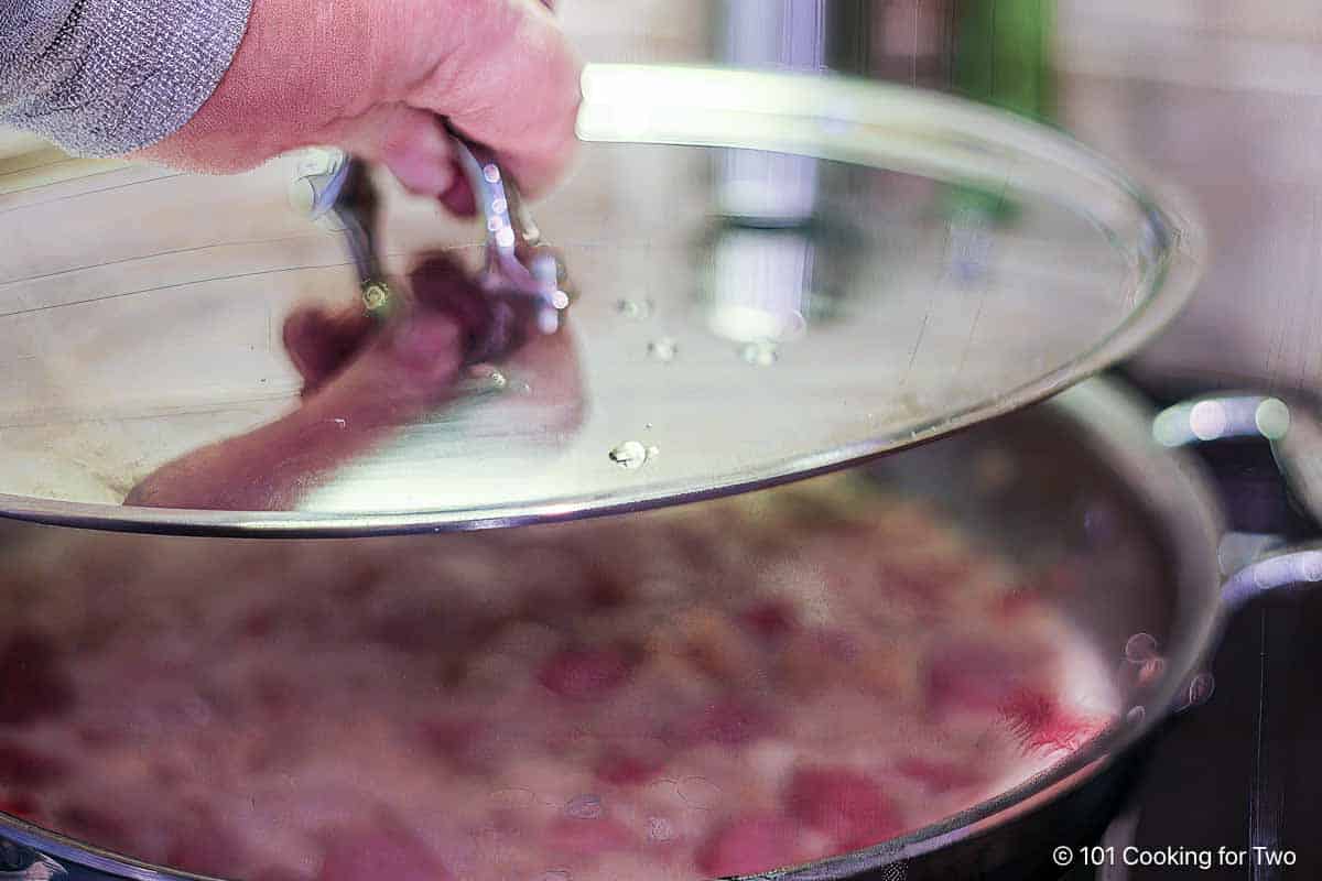 Covering the pan with a lid to simmer.