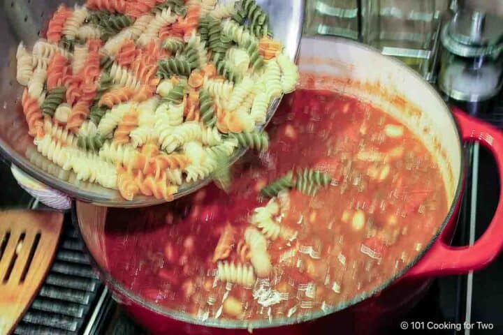 Pouring pasta into soup.