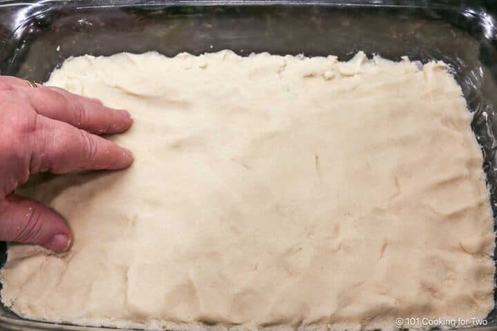 Pressing the shortbread into a baking dish to make the crust.