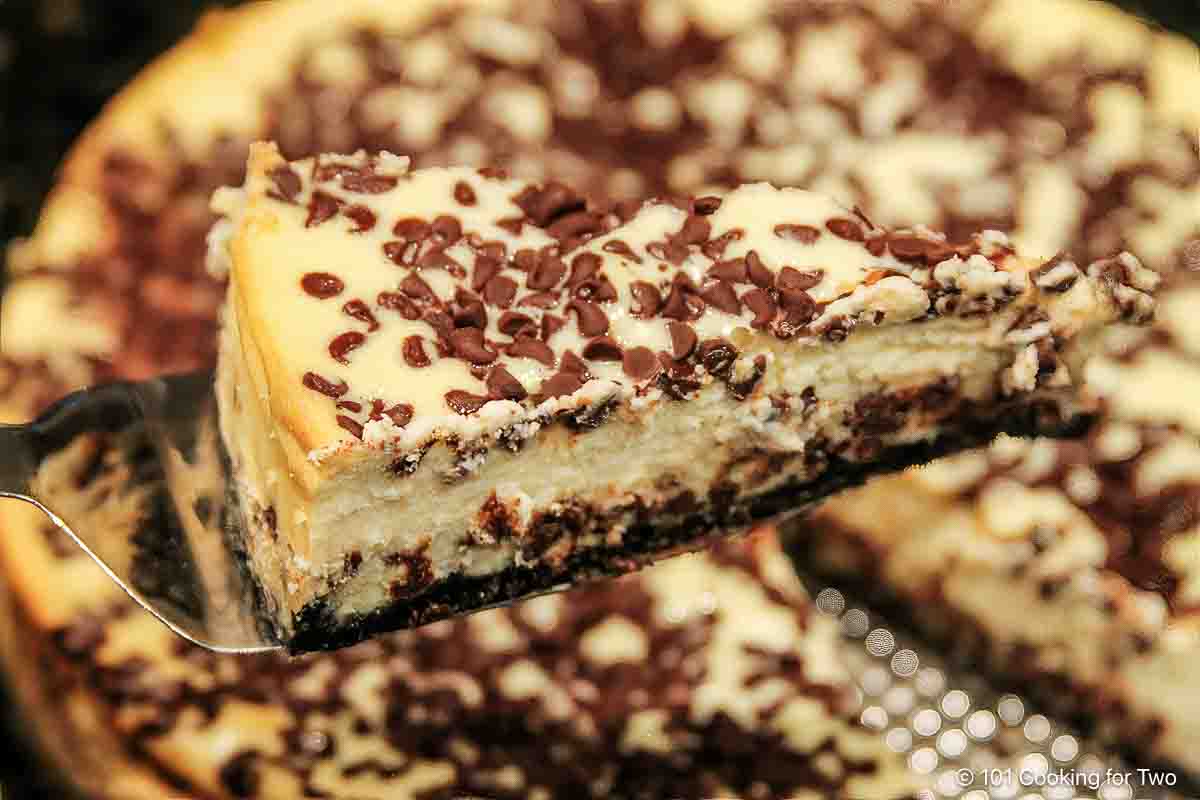 Slice of chocolate chip cheesecake on a spatula over the cheesecake.