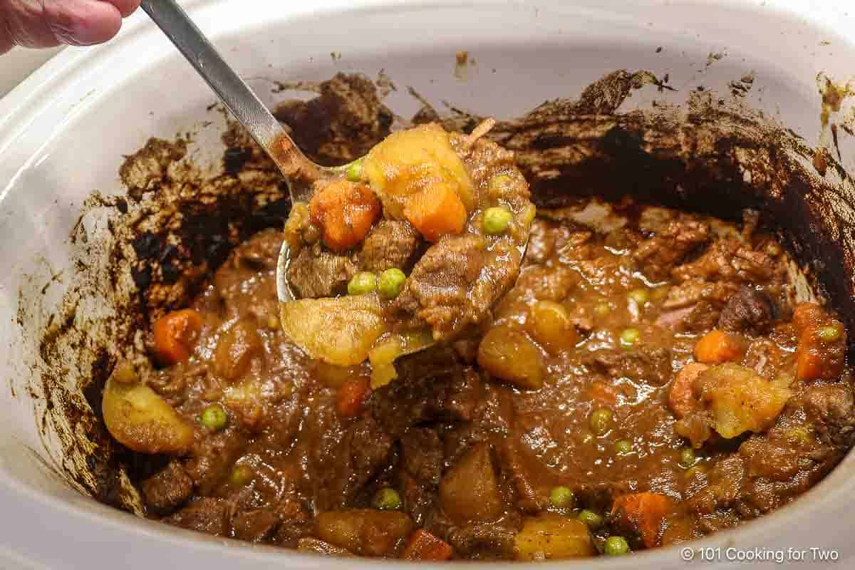 Beef stew in a ladle over the crock pot.