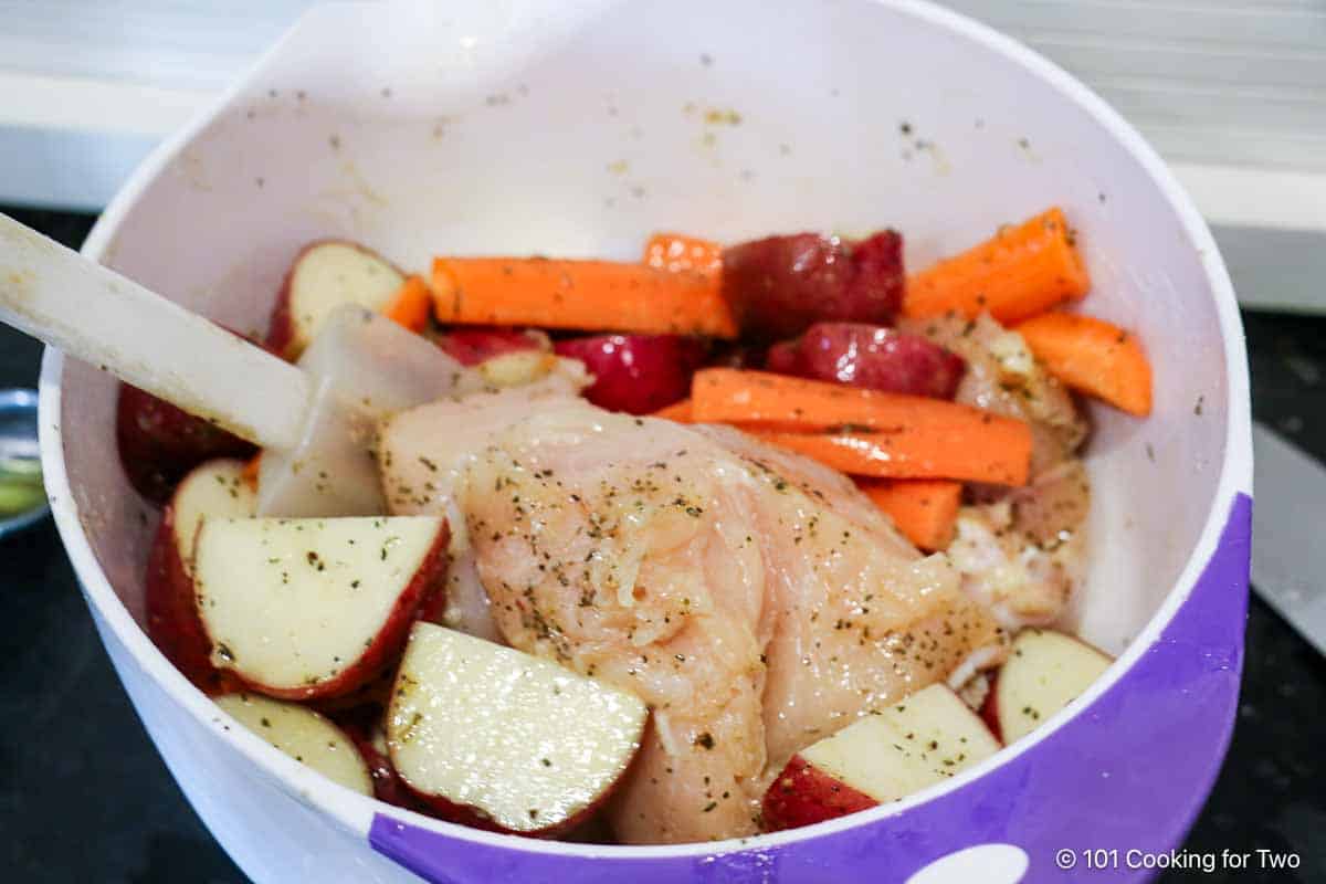 Coating the chicken and veggies with oil and seasoning.