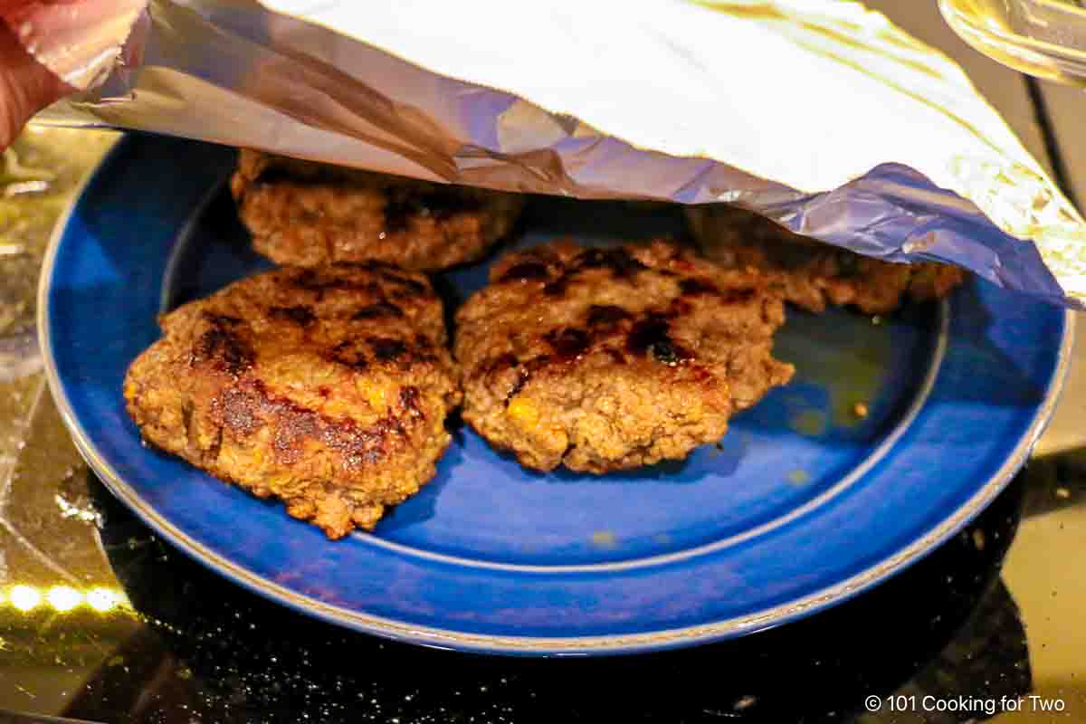 Tenting cooked patties on a plate.