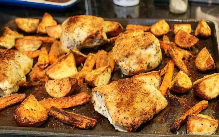 Tray of cooked chicken with potatoes and carrots.