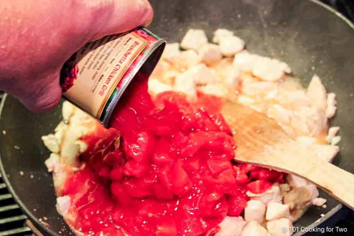 Adding diced tomatoes to the chicken.