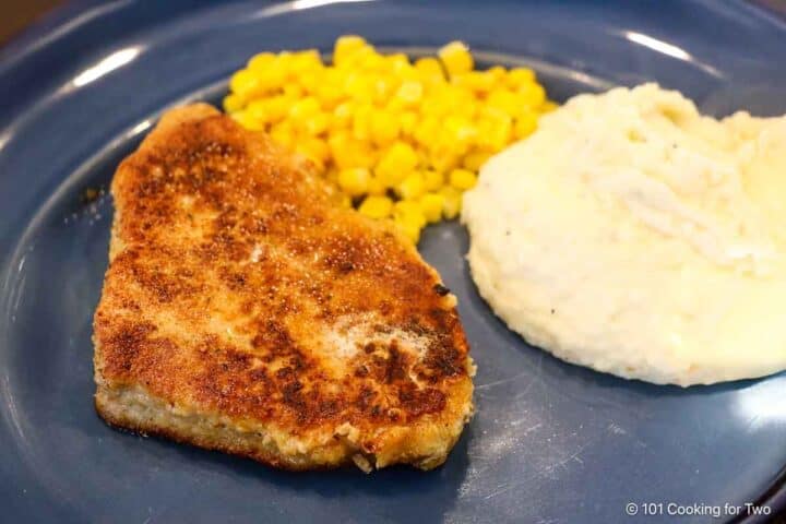 Breaded pork chop on a plate with corn and potatoes full.