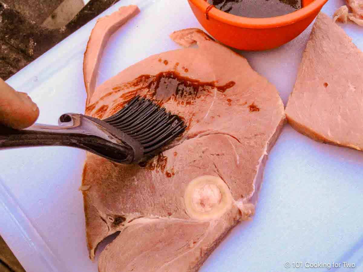 Brushing the ham steak with brown sugar glaze.