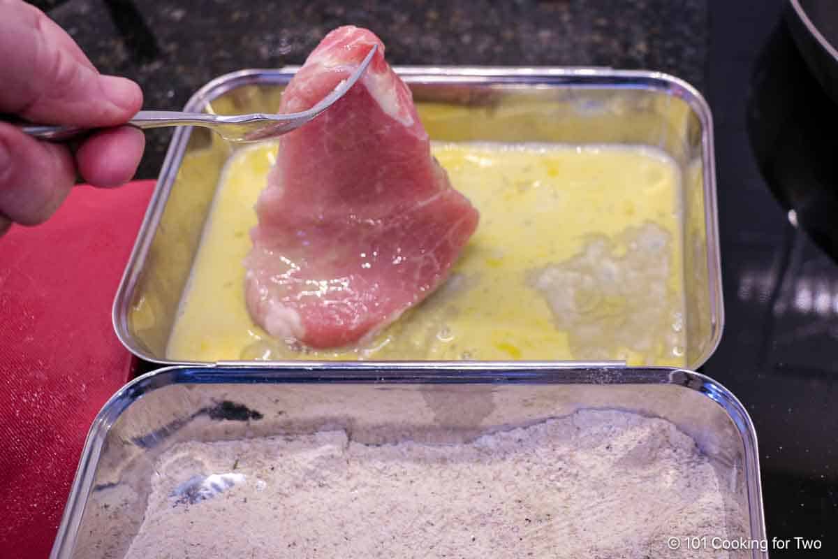 Coating a pork chop with egg wash.