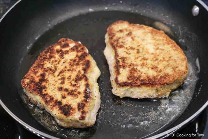 Flipped breaded pork chops in a pan.