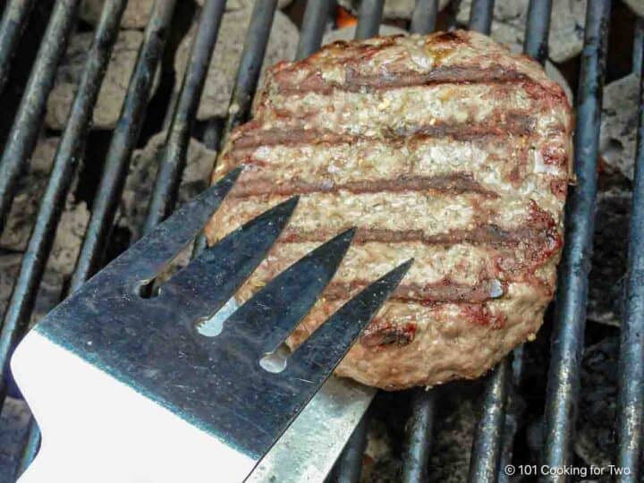 Flipping a burger pattie on a grill.