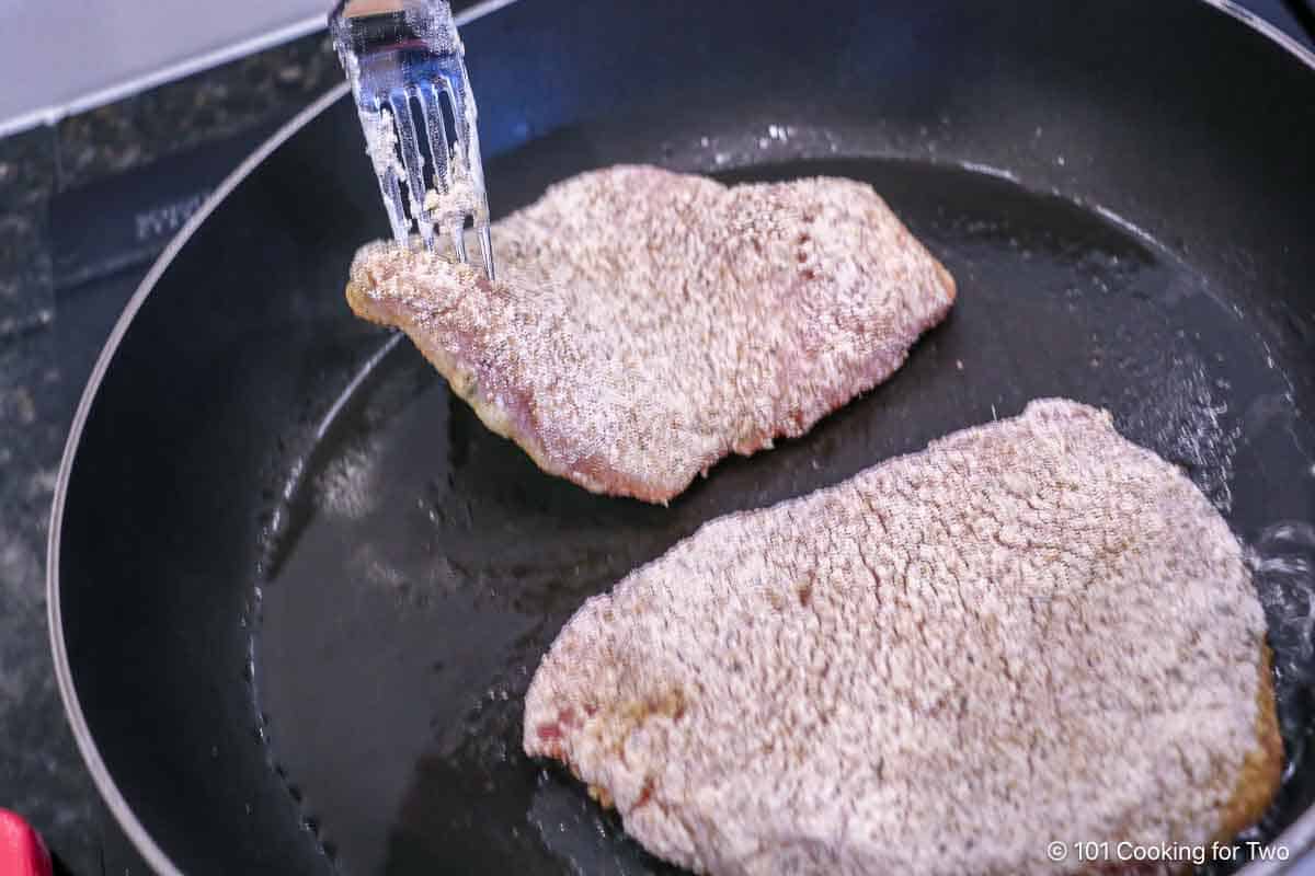 Laying a breaded pork chop into a hot frying pan.