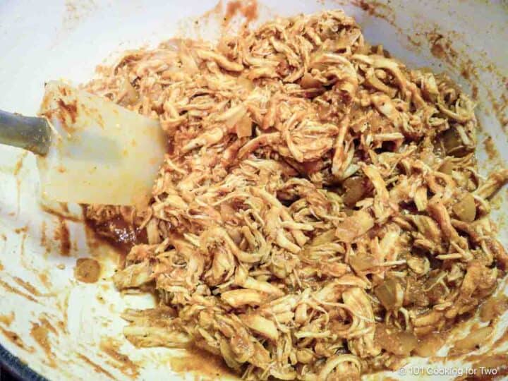 Mixing shredded chicken with tomato sauce.