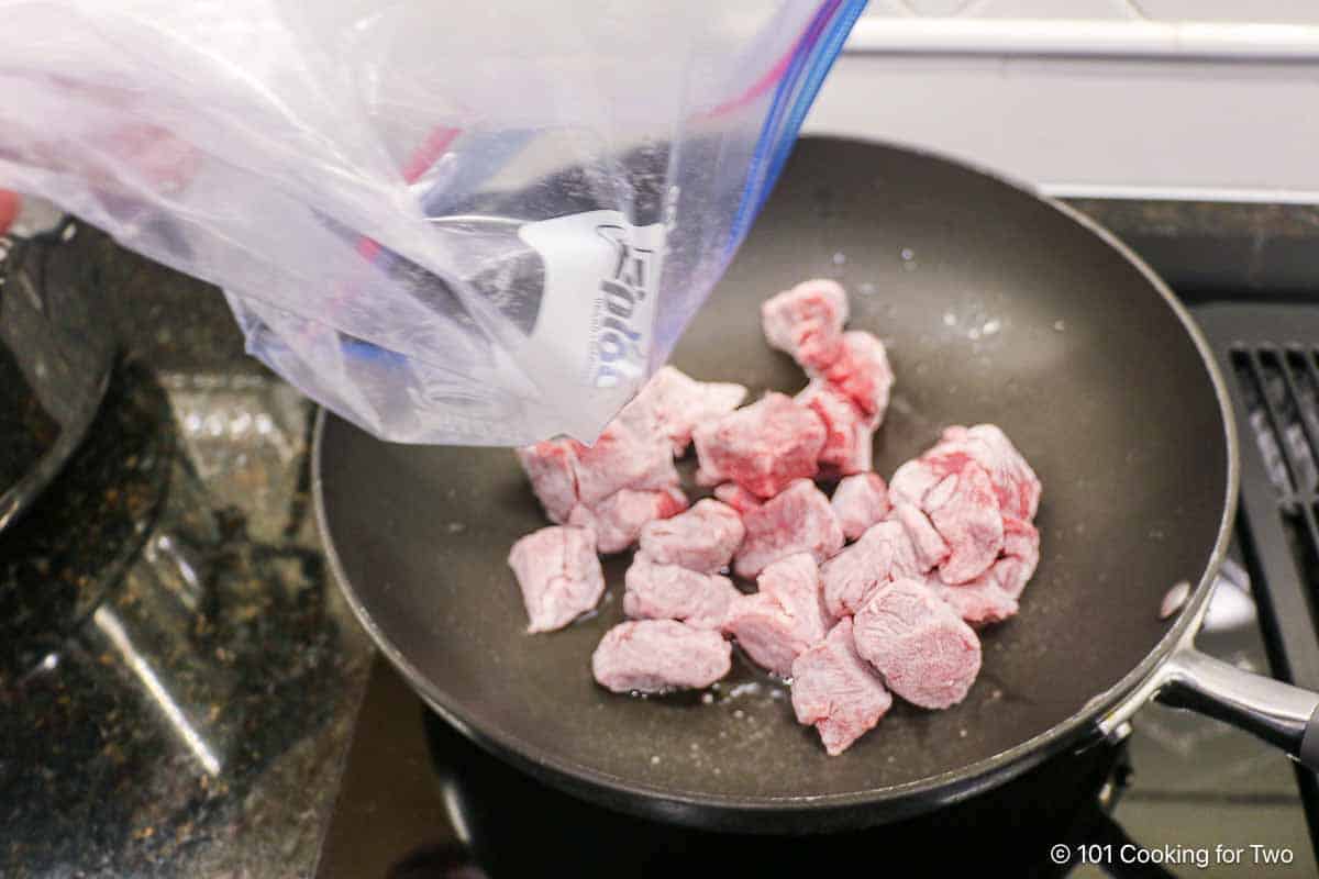 pouring floured stew meat to a pan with hot oil