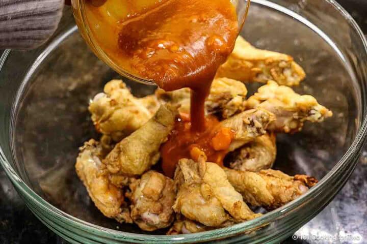 Adding coating sauce to baked wings.