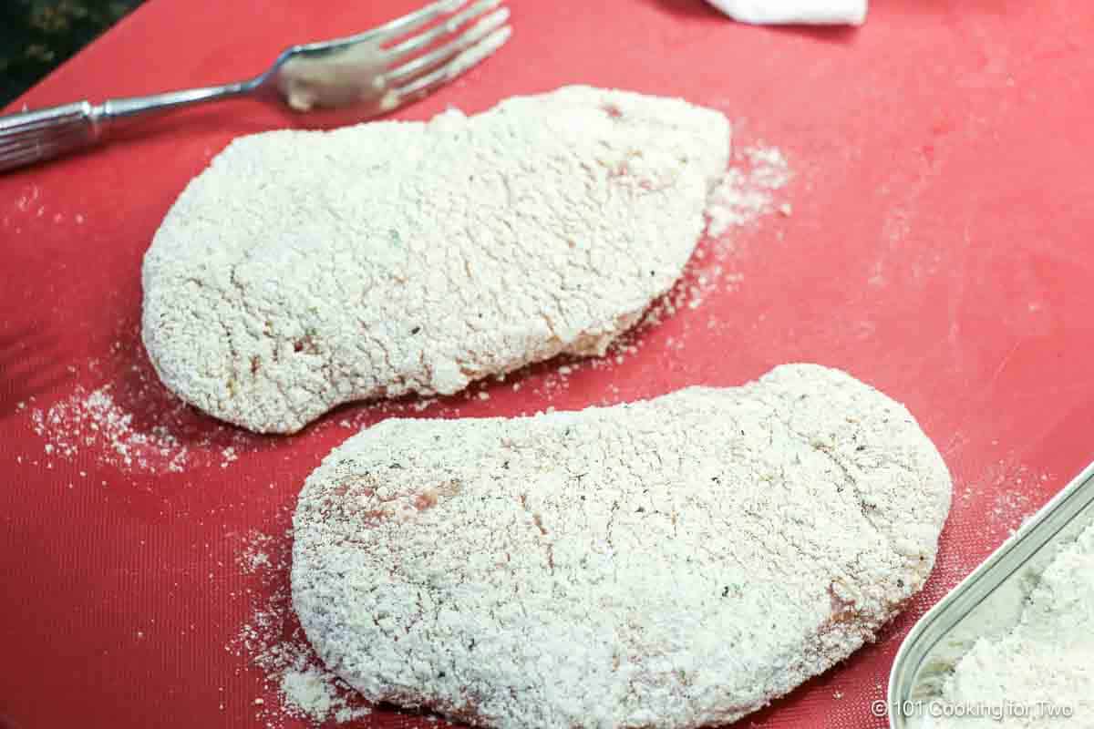 Resting uncooked breaded pork chops on a board.