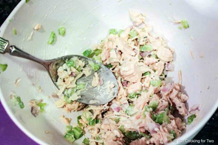 Mixing chicken salad in a white bowl.