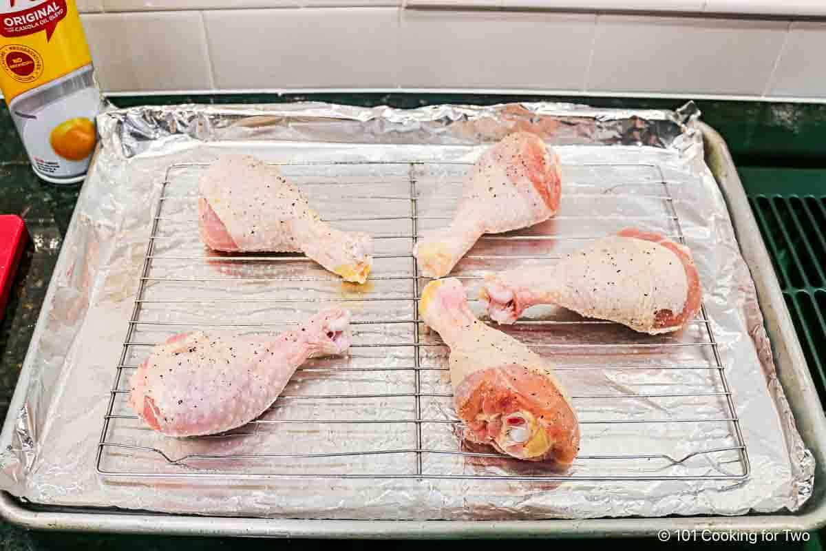 Raw chicken legs on a rack and baking tray.