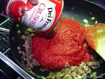 Adding crushed tomatoes to the browned meat.