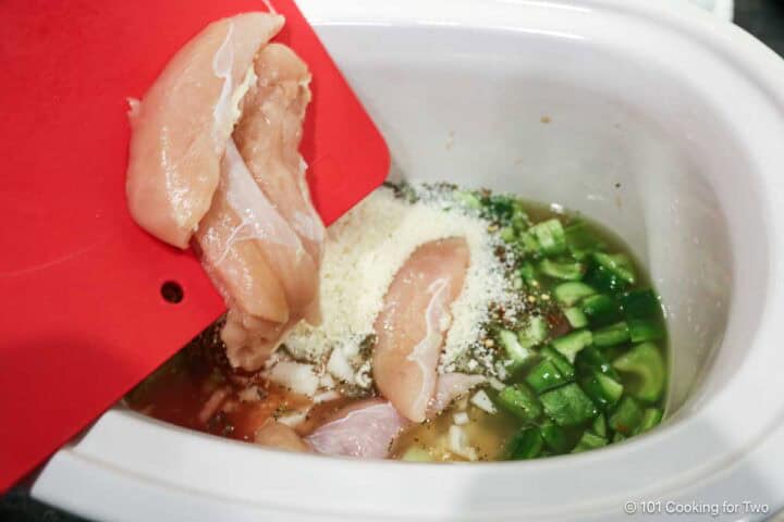 Adding trimmed chicken to the crock pot with other ingredients.