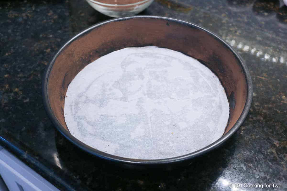 Preparing baking pan with parchment paper in the bottom and cocoa and butter on the sides.